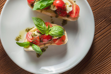 bruschetta with cherry tomatoes, basil, pesto sauce and mozzarella on a white plate on a wooden background. Italian restaurant. Top view food photo