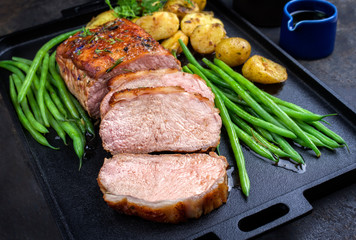 Traditional roasted dry aged veal tenderloin with beans and potatoes offered as closeup on a modern design cast iron tray