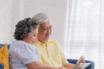 Asian senior couple use tablet video conference with doctor about pill  while sitting on sofa at home,senior learn to use technology.aging at home