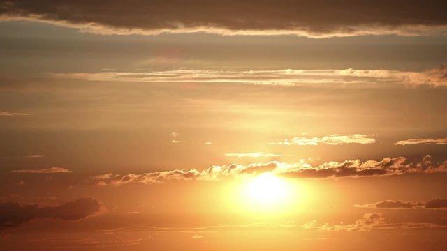 Close up time lapse of bright shining setting sun. Beautiful epic scenic cumulus clouds rolling over sky background backlit by sunset.