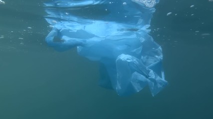 Plastic pollution, discarded blue plastic bag drifting underwater in the blue surface of water. Underwater shot