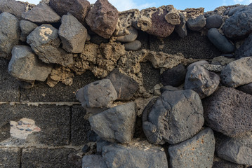 An old wall that collapses from time to time, made of lava brick and decorated with cobblestones that partially fell off, exposing the plumes of cement mortar