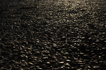 Wet from the surf smooth black pebbles from lava glare in the setting sun