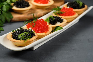 tartlets with red and black caviar on a white plate with lemon on a gray background. Close-up