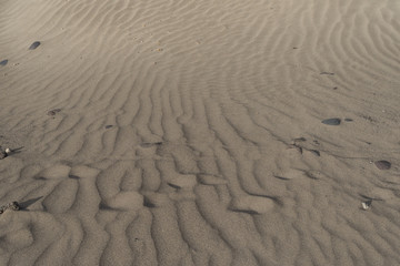 Dry sand gracefully laid with strong wind strips stretching into the distance and horizontal line of human traces swept up by the wind