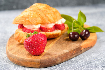 croissant sweet sandwich with cream cheese and strawberries on a wooden board and gray background. Useful breakfast. Proper nutrition. French traditional dishes.