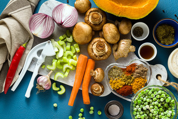 Fototapeta na wymiar Ingredients for cooking Indian curry from vegetables, pumpkins and mushrooms on a blue background and spices. shot from above. copy space