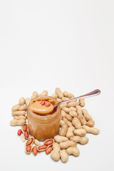 Creamy peanut butter in glass jar, peanut and spoon isolated on white background. A traditional product of American cuisine