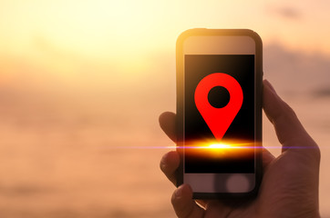 Copy space man hand using black smart phone on sunset beach background with navigator gps location icon. Travel adventure lifestyle and business economic concept.