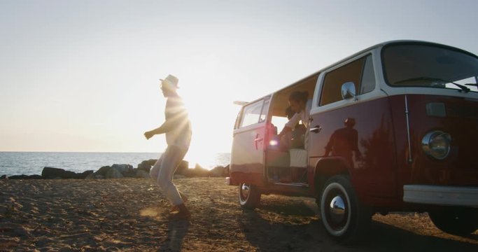 Slow motion of group of young multi-ethnic friends just arrived with a minivan are happy to start their vacation  and having fun on a beach with a sea on a sunset.
