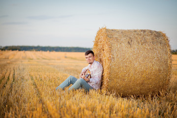 Naklejka na ściany i meble young guy is relaxing in the countryside with a guitar. Plays the guitar . Resting lying on the hay