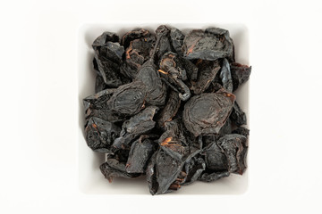 Prunes in white saucer on white background. Top view