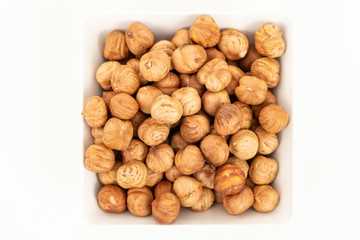 peeled hazelnuts in a white bowl on a white background. Top view