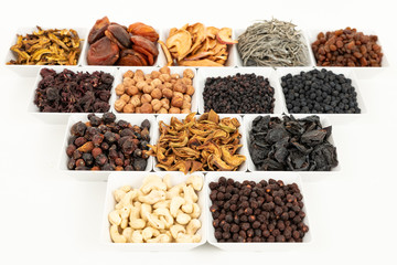 Groups of various kinds of dried fruits in square white bowls on white background