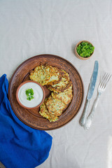 Zucchini fritters, vegetarian zucchini pancakes, served with fresh herbs and sour cream, top view. Light background.