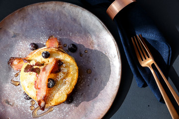 american pancakes with bacon and blueberries with bronze knife and fork and blue napkin
