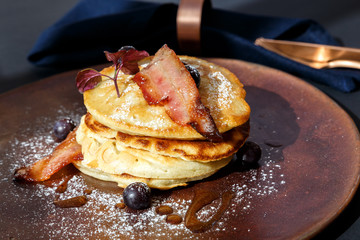 american pancakes with bacon and blueberries with bronze knife and fork and blue napkin
