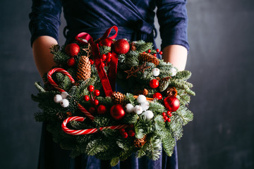 Festive floral arrangement. Cropped shot of lady in blue dress holding Christmas wreath decorated...