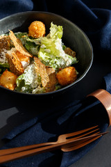 chicken caesar salad in a bowl with blue napkin and bronze knife and fork