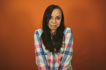 A beautiful woman in a plaid shirt poses on an orange background.