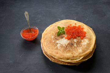 Stack of pancakes with red caviar on dark rustic background, top view