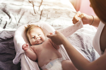 Obraz na płótnie Canvas Mom dresses a newborn baby, buttoning up a jumpsuit. Home comfort.