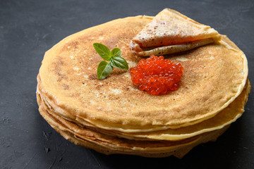 Stack of pancakes with red caviar on dark rustic background, close up