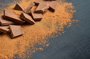 Heap of broken pieces of milk or bitter chocolate powdered of cocoa scattered on dark scratched concrete table. Space for text