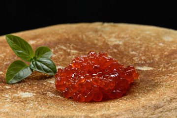 Stack of pancakes with red caviar on black background, close up