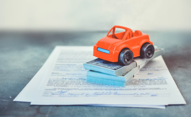 Buying a car concept with little toy car, dollars and documents