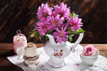 bunch of pink dahlia in porcelain jug on wooden table