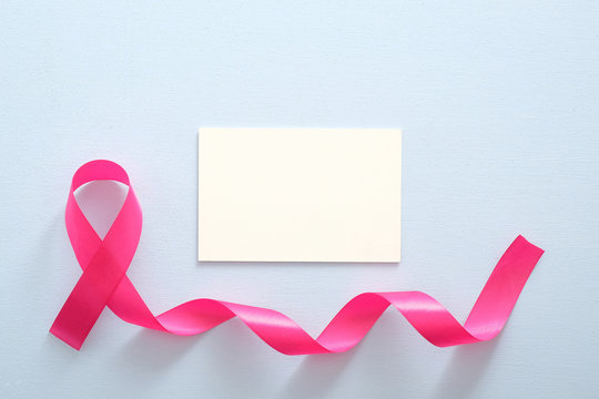 Breast cancer awareness month concept. Empty paper card mockup and pink breast cancer ribbon on blue background.