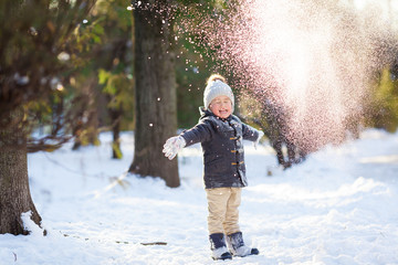 Happy 4 years old boy having fun in the park throws snow and laughs.