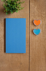 Flat layout of a blue book and two heart shape stamps on a wooden desk background.