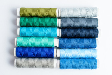 Two lines  of colourful blue spools of thread displayed vertically, isolated on white, top view