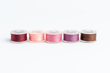 Five spools of burgundy, light pink, pink, mauve and brown threads prepared for the sewing machine,...