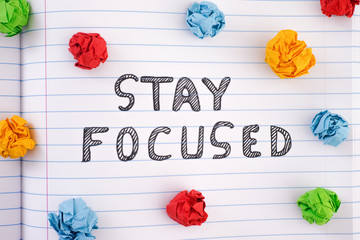Phrase Stay Focused on notebook sheet with some colorful crumpled paper balls around it
