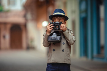A boy of 7 years old wearing a vintage cloak and hat holds in his hands an old camera 