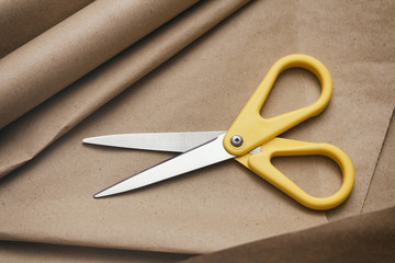 Yellow scissors on craft brown paper texture background. Packaging process. Gift and flowers shop. Shipping service. 