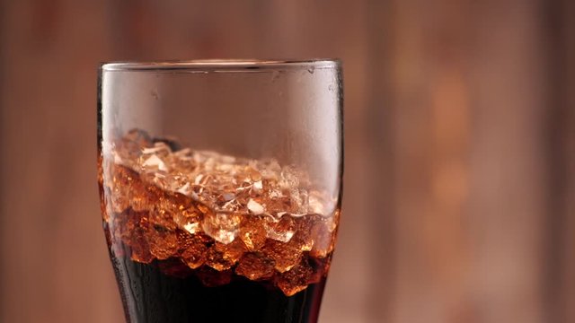 Full glass of cola with ice. Someone puts it in the frame in slow motion.