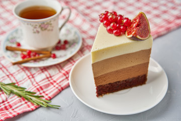 A piece of homemade cake decorated with red currants, figs, cinnamon and rosemary with a tablecloth, Cup and saucer on a light background concrete table.