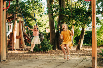 Funny kids playing on playground, little girls having fun on swing