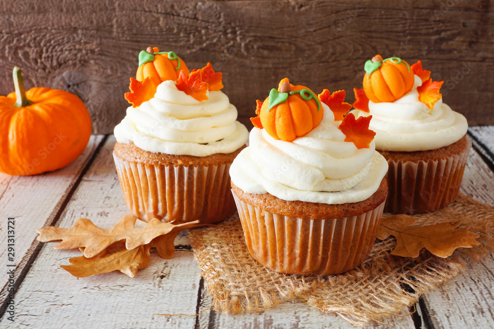 Poster fall pumpkin spice cupcakes with creamy frosting and autumn toppings. close up against a rustic wood