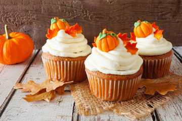 Fall pumpkin spice cupcakes with creamy frosting and autumn toppings. Close up against a rustic...