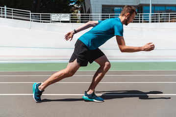 Fototapeta premium side view of athletic young sportsman jogging on running track
