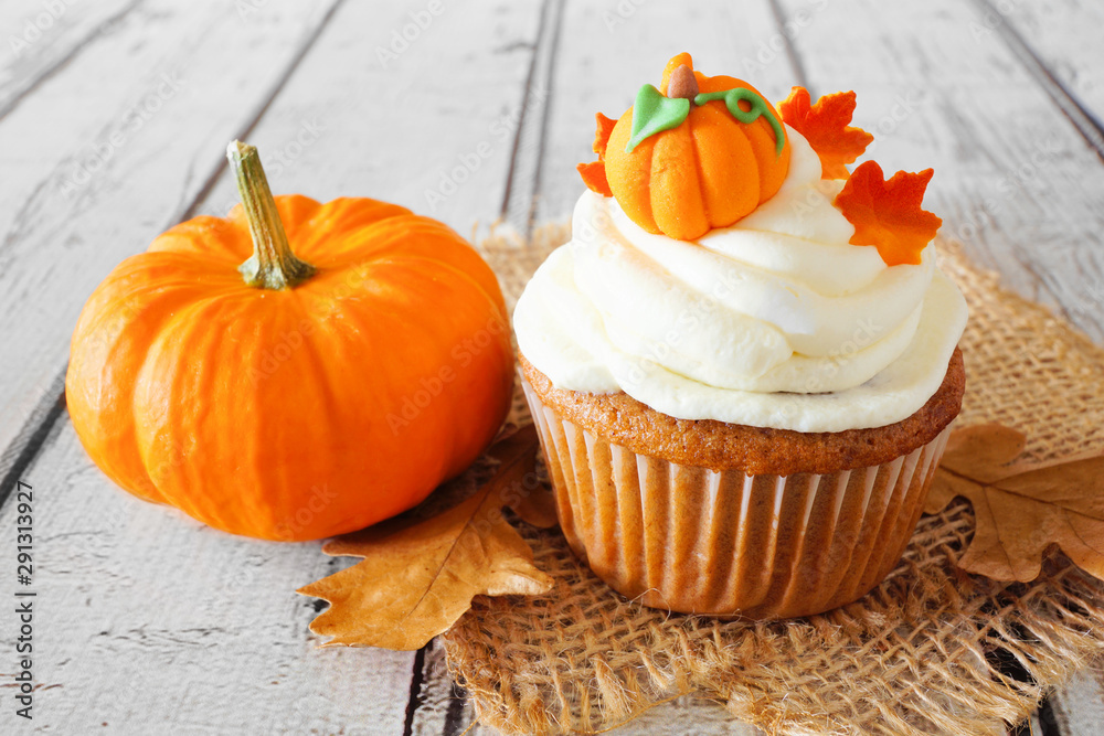 Poster fall pumpkin spice cupcake with creamy frosting and autumn toppings close up on a rustic white wood 