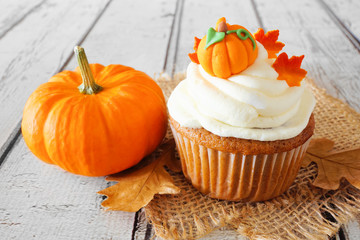 Fall pumpkin spice cupcake with creamy frosting and autumn toppings close up on a rustic white wood...