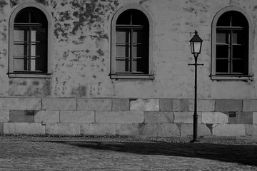 Concrete wall with three windows and one street lamp. Old historic building atmospheric monochrome image. 