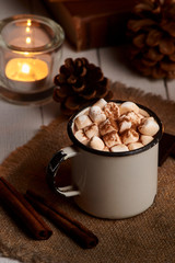 Cup of hot cocoa or hot chocolate with marshmallows and cinnamon sticks on wooden background with burning candles. Rustic. Winter mood. Vertical