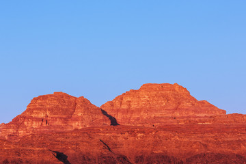 Jordania: top of the rock mountains in the Wadi Rum desert during sunrise. Soft red and orange colors, and soft blue sky.
